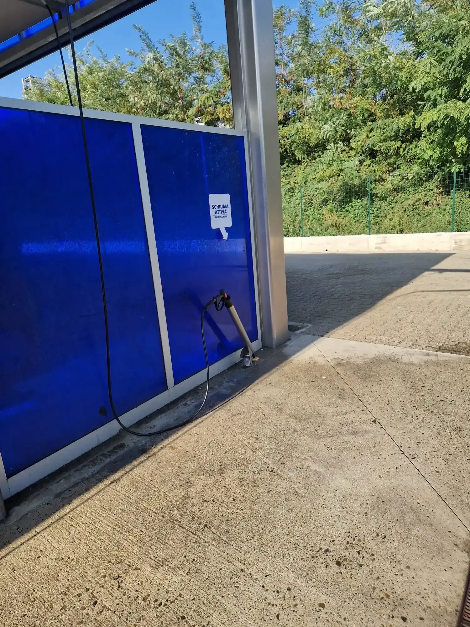 Autolavaggio blu con tubo flessibile, in una giornata di sole. Pavimento in cemento.