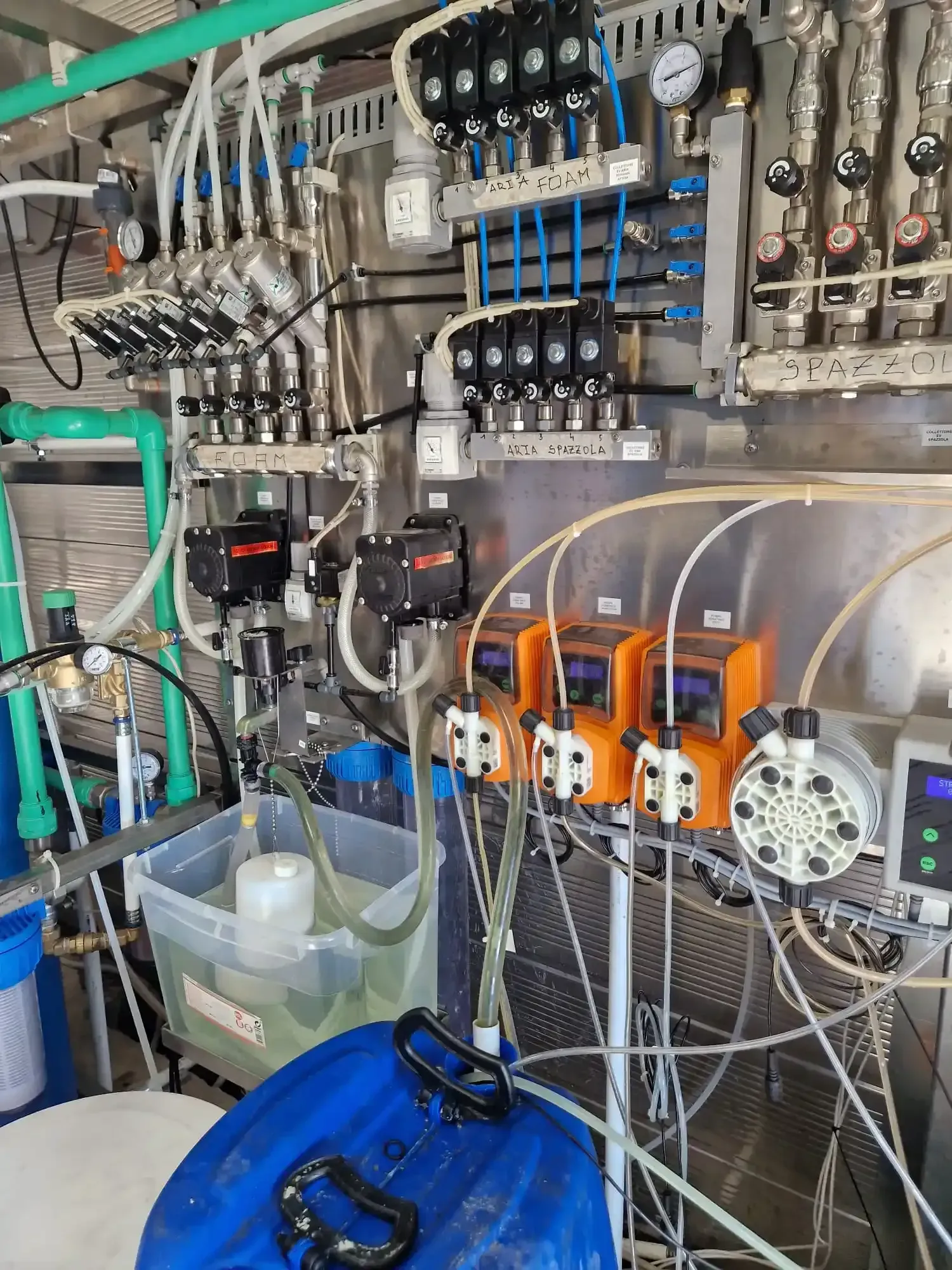 Apparecchiature industriali complesse con tubi, pompe e comandi. Pompe arancioni, serbatoi metallici e barile blu.