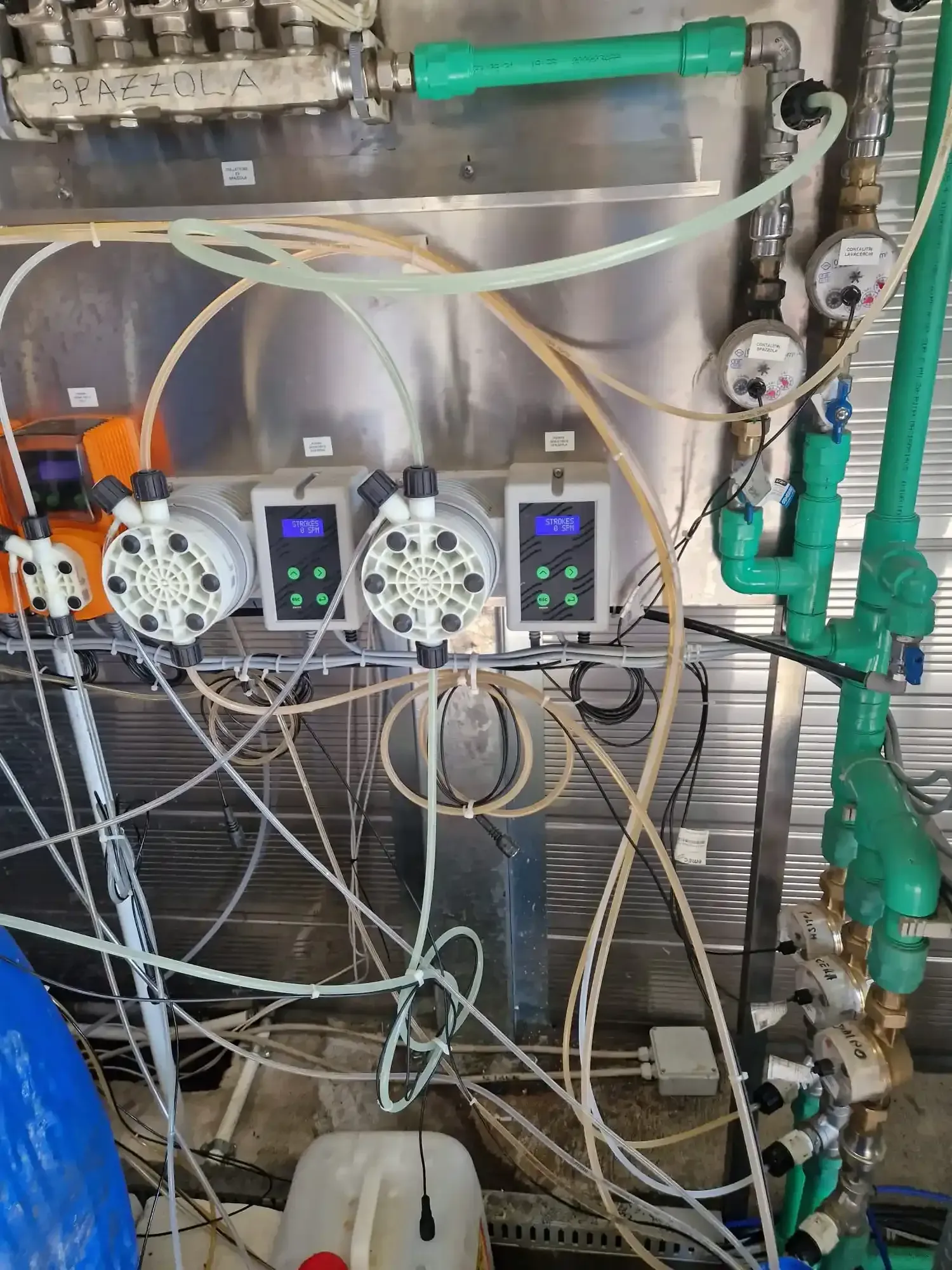 Attrezzatura industriale con pompe, manometri e tubi; uno sfondo con pannello metallico.