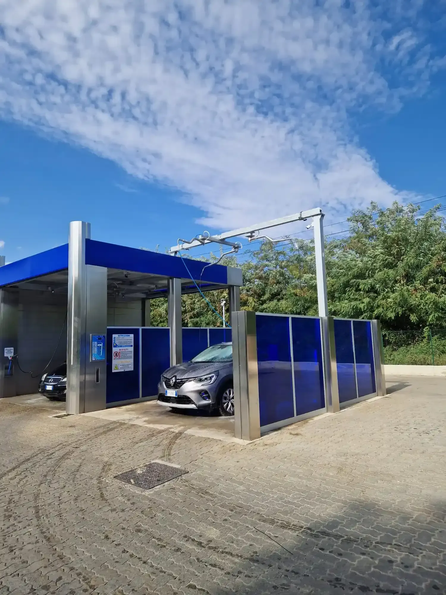 Auto lavata in un autolavaggio automatico con dettagli blu e argento, sotto un cielo soleggiato.