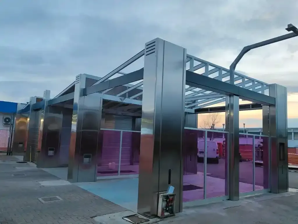 Autolavaggio con colonne in acciaio inox, pareti rosa e cielo azzurro.