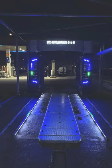 L'ingresso di un autolavaggio illuminato di notte con luci blu, sullo sfondo si vede una stazione di servizio.