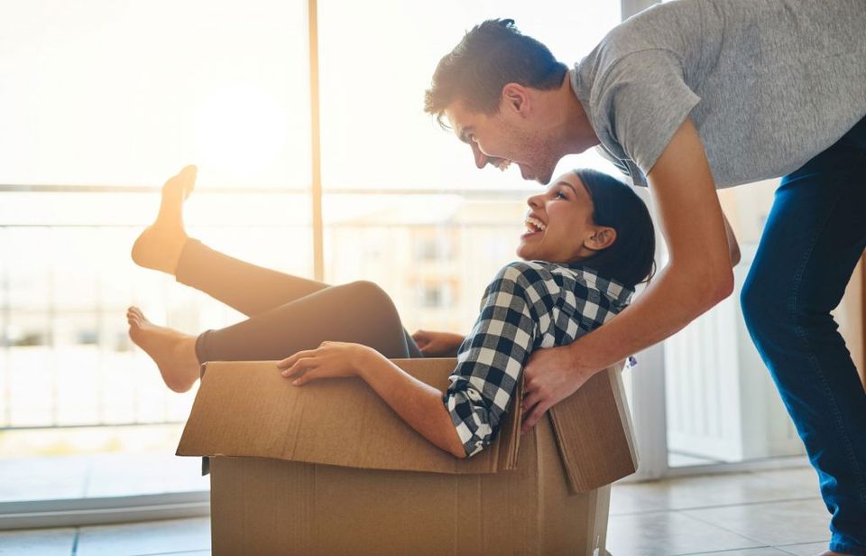 Shot of a young man pushing his girlfriend around in a box while they move into their new home together