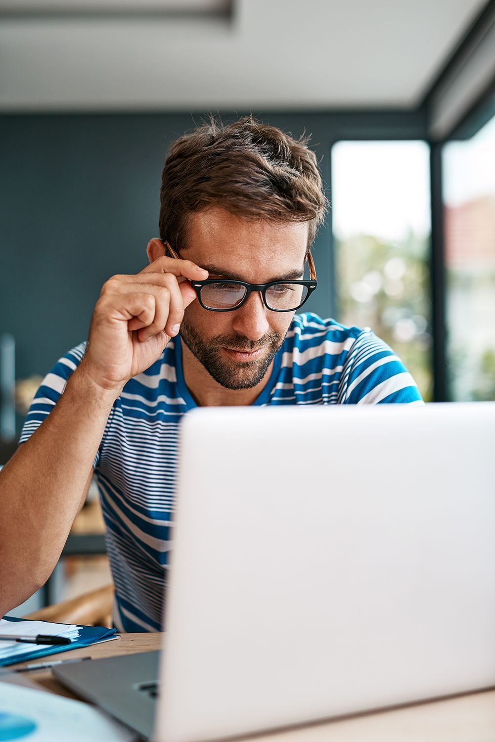 a man wearing glasses is looking at a laptop computer .