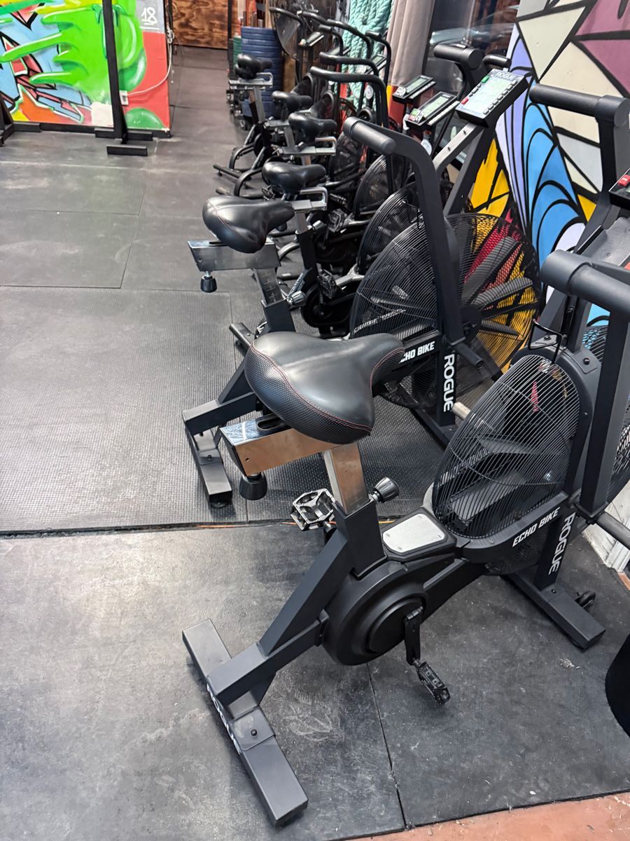 Row of stationary bikes in a gym, black frames and seats, on a dark floor.