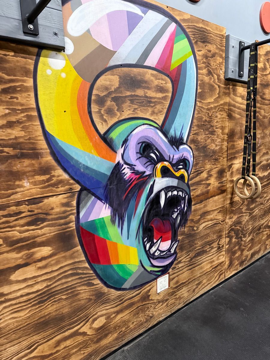 Colorful gorilla head inside a kettlebell shape, painted on a wooden wall.
