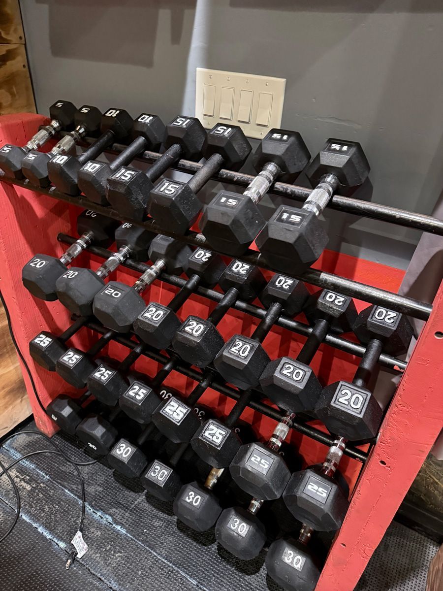 Dumbbell rack with various weights: 5-30 lbs, black weights on a red rack, gray background.