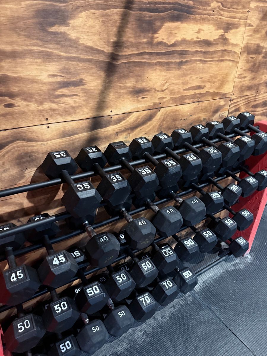Dumbbell rack with various weights, including 45s, 50s, and 35s, against a wood background.