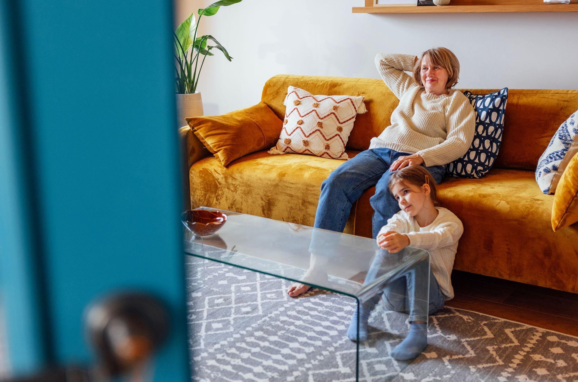 A woman and a child are sitting on a yellow couch in a living room.