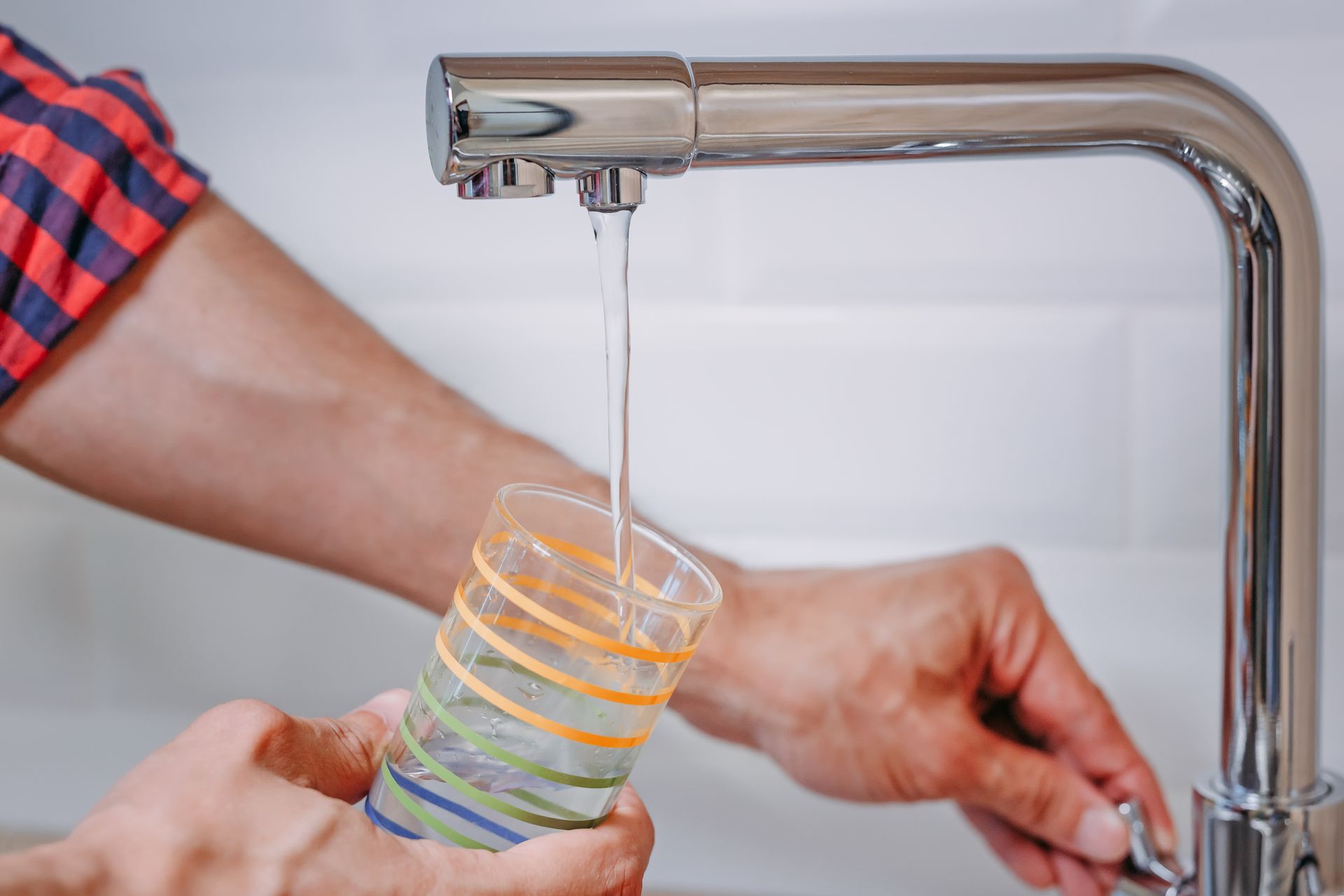 A person is pouring water into a glass from a faucet.