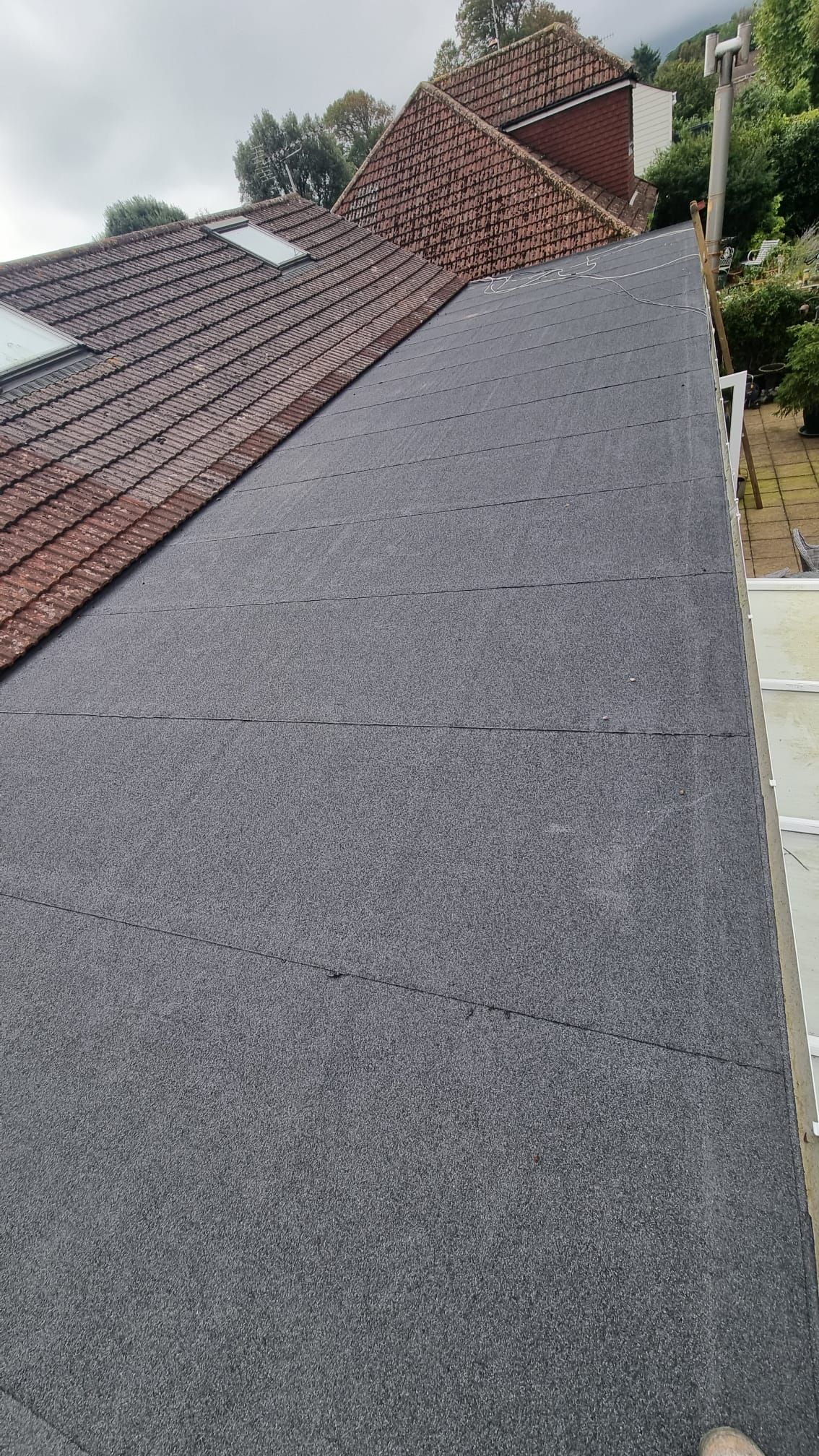 A person is standing on the roof of a house with a black roof.