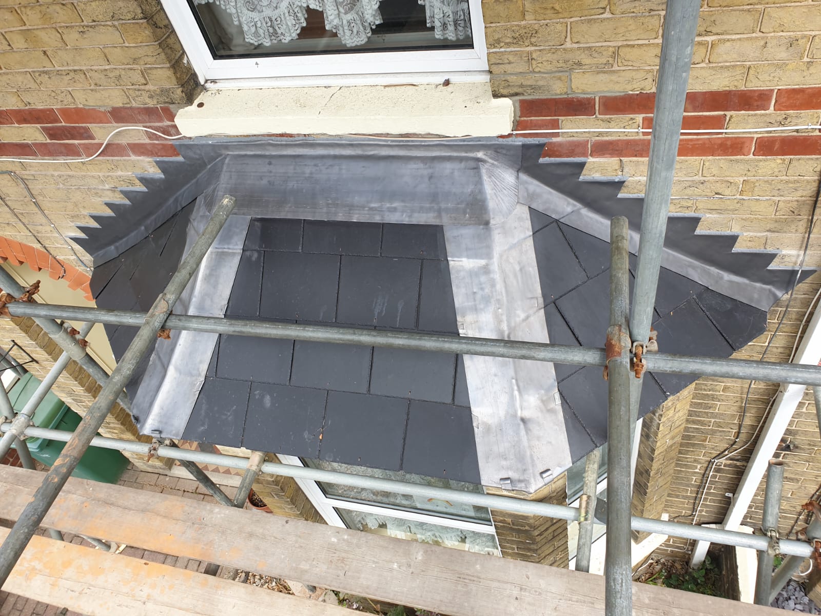 A scaffolding is sitting on top of a brick building next to a window.