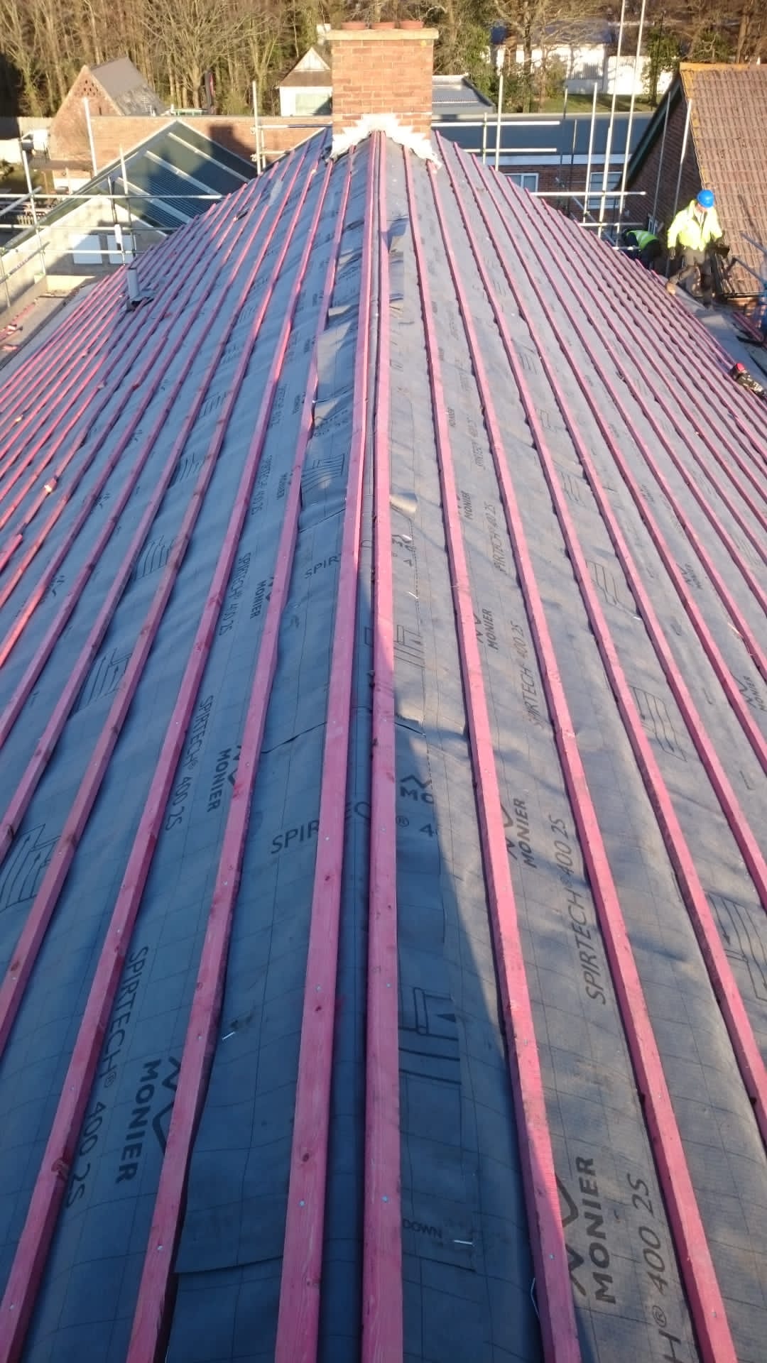 The roof of a building is being covered with red shingles.