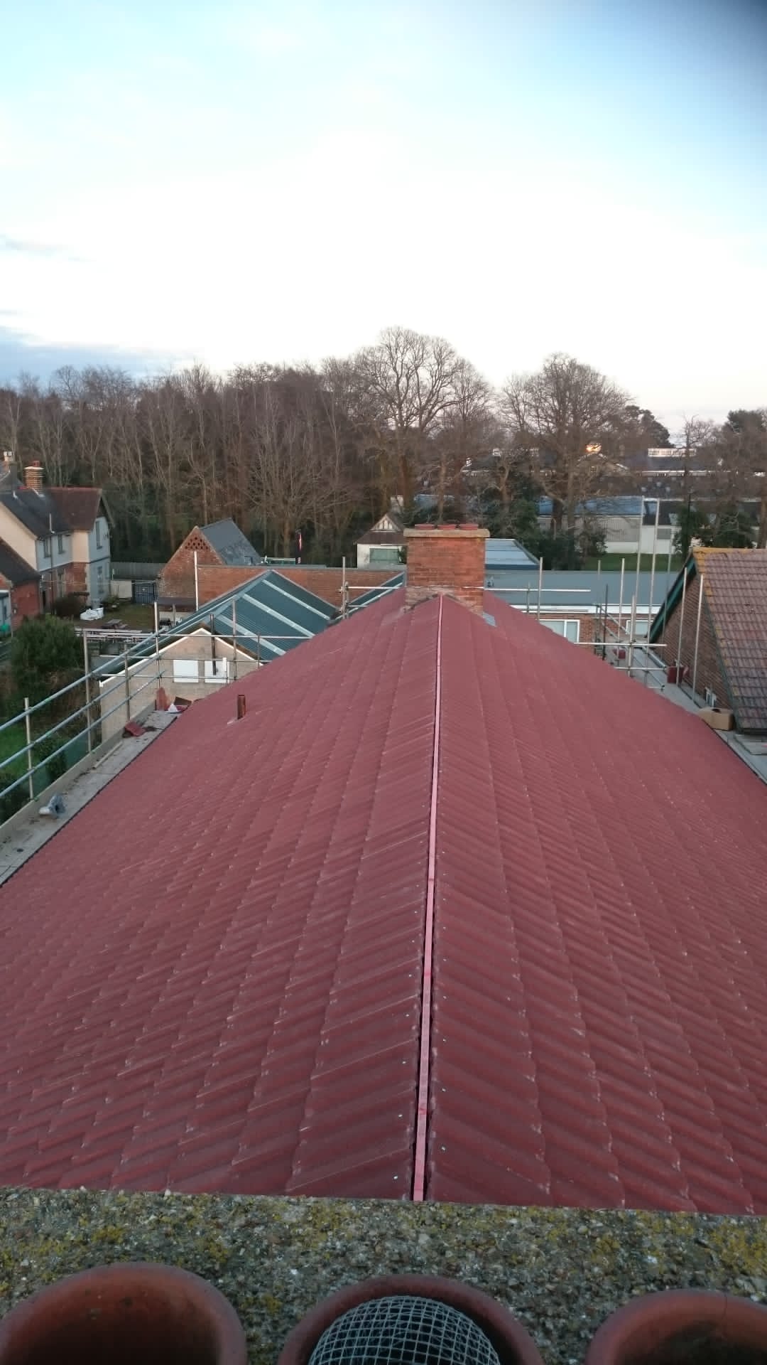 The roof of a building with a red roof and trees in the background.