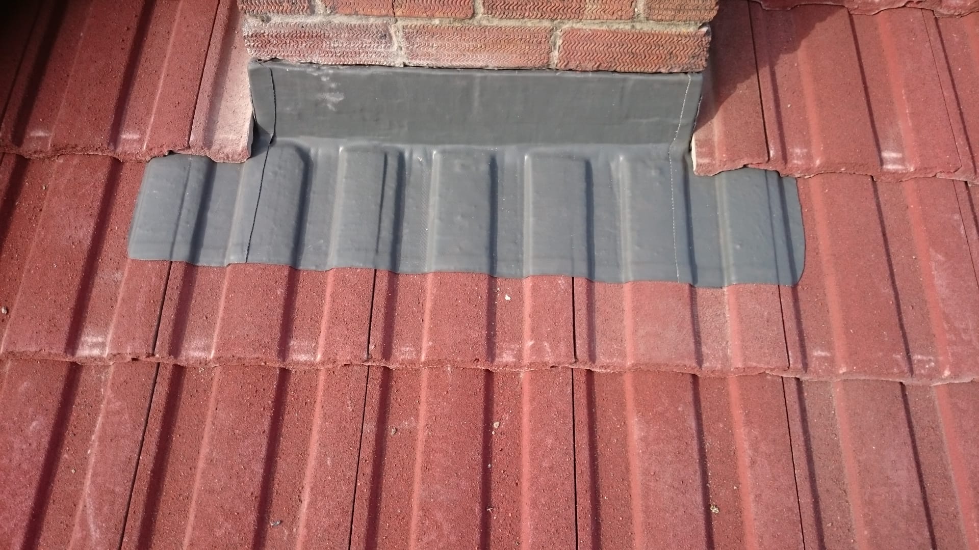 A chimney is sitting on top of a red tiled roof.