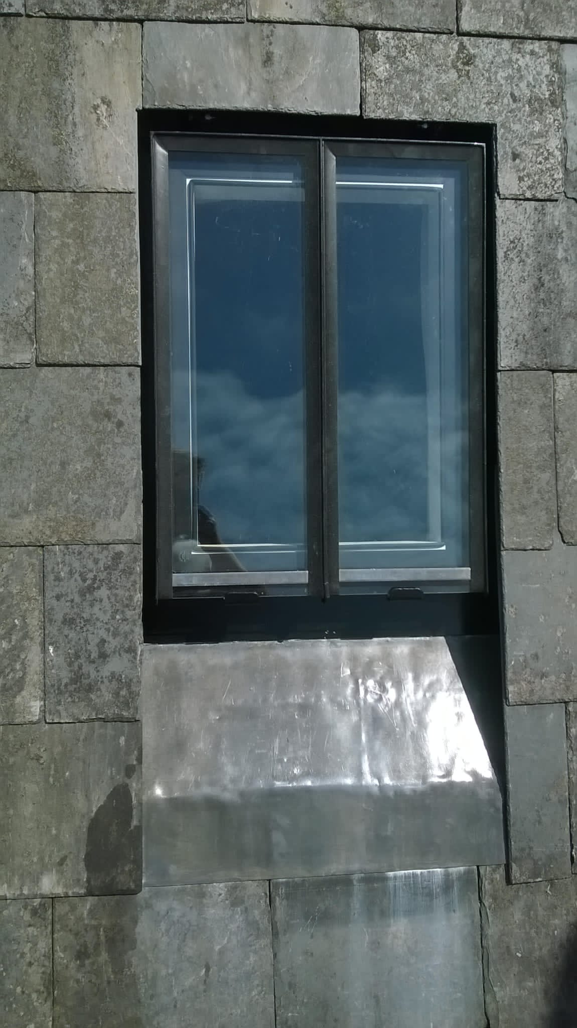 A window with a black frame is on a brick wall.