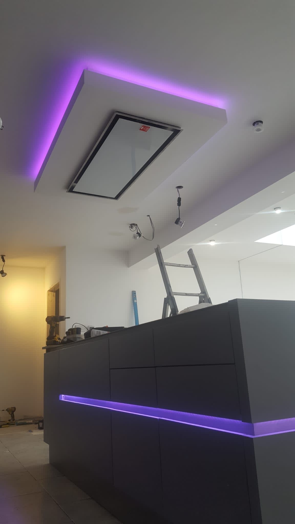A kitchen with purple lights on the ceiling and a ladder.