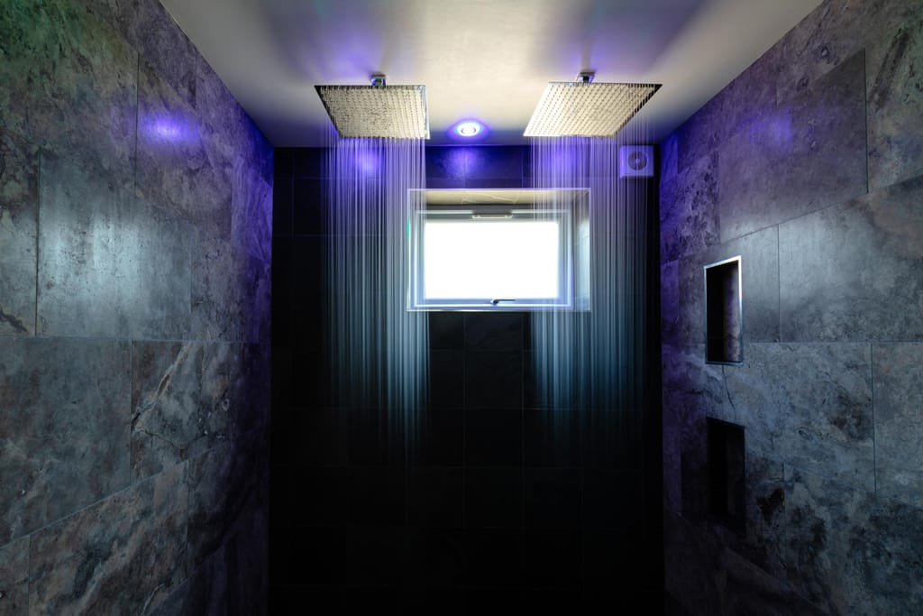 A shower with purple lights on the ceiling and a window.