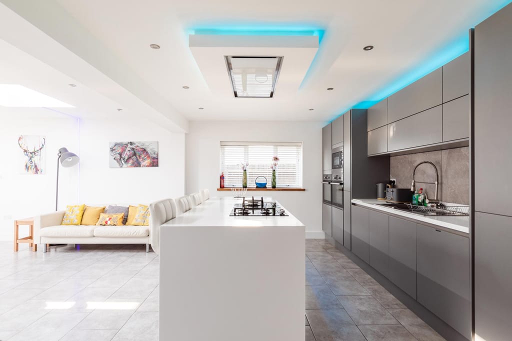 A living room with a couch and a kitchen with a blue light on the ceiling.