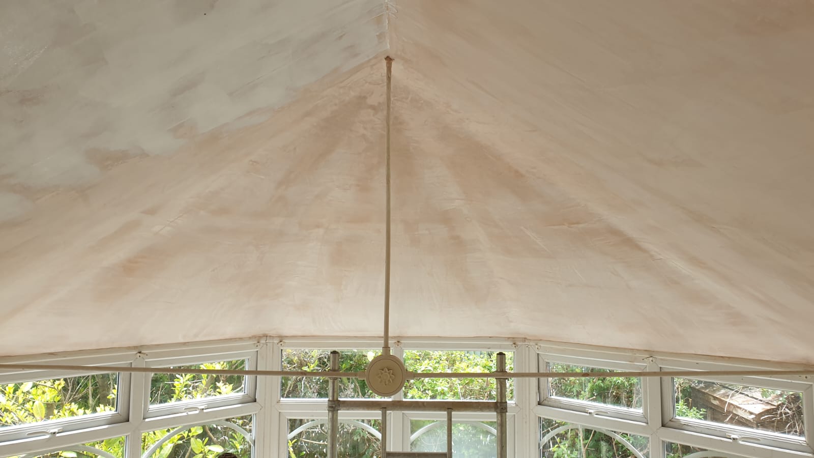 A ceiling fan is hanging from the ceiling of a room with lots of windows.