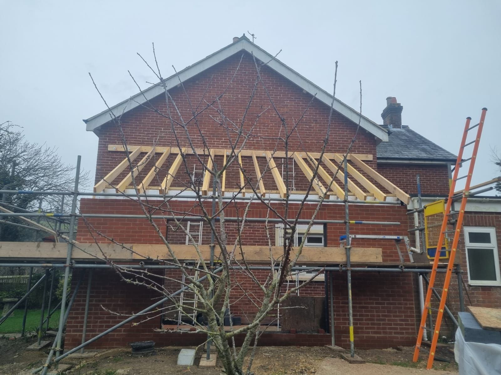 A brick house is being built with scaffolding and a ladder.