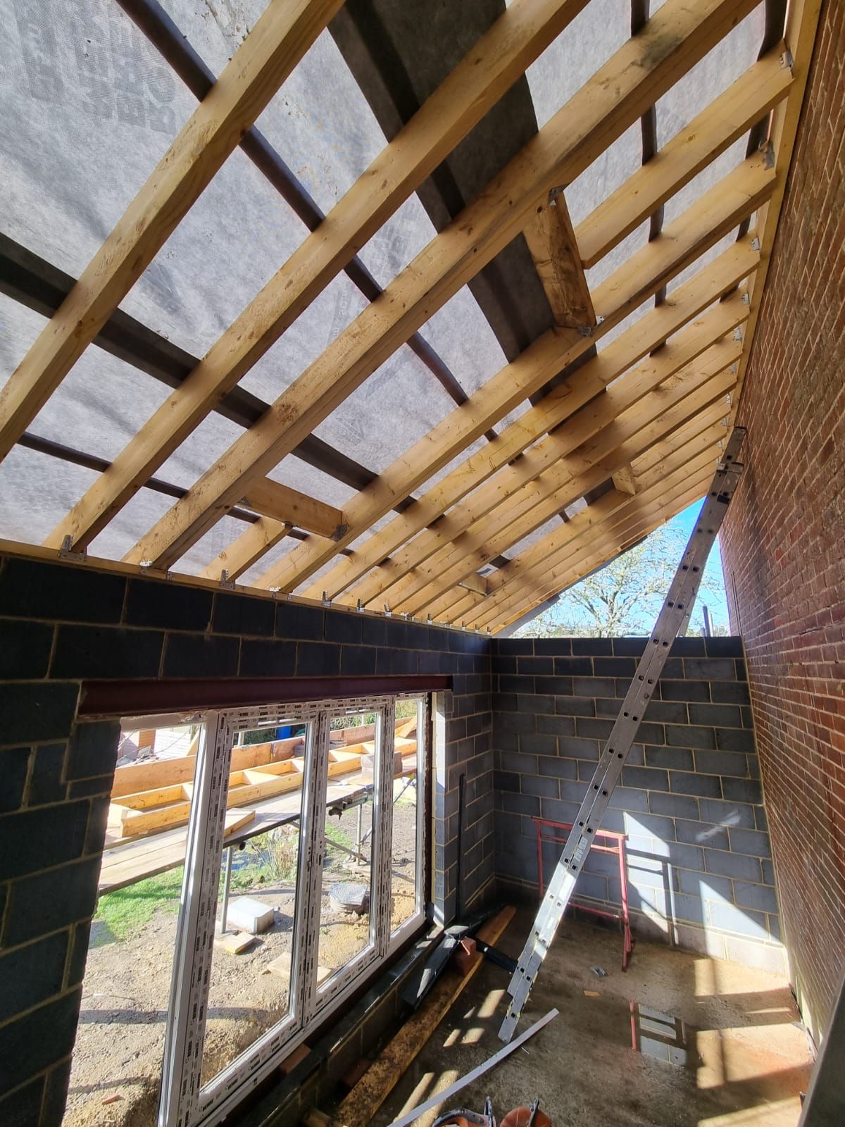 a room under construction with a wooden roof and a ladder .