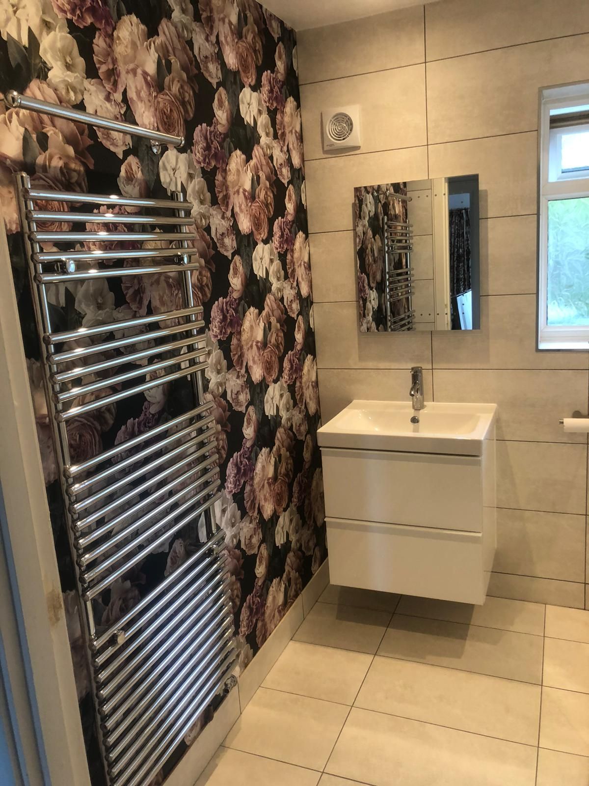 A bathroom with a sink , towel rack , mirror and floral wallpaper.