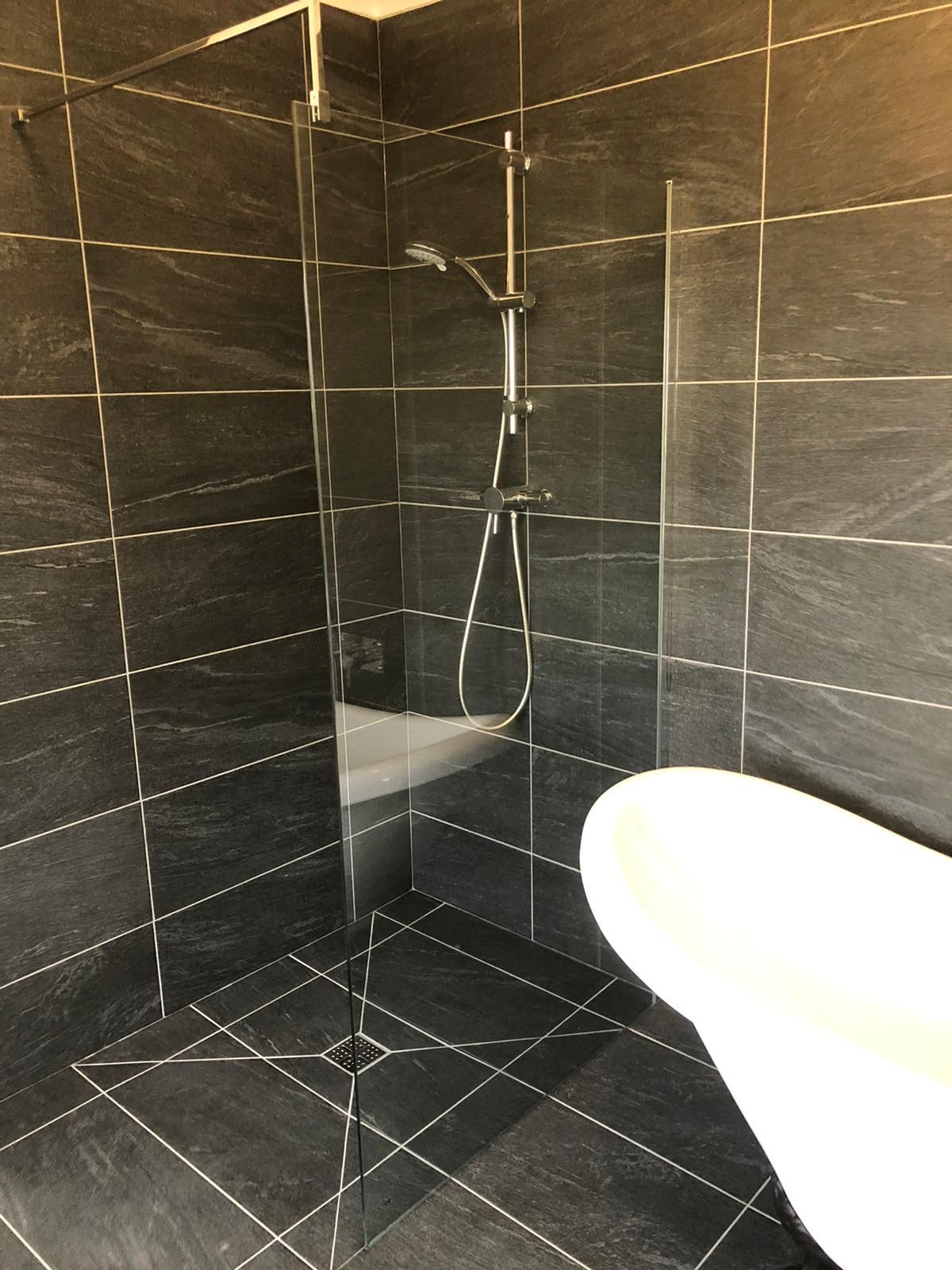 A bathroom with black tiles and a walk in shower.