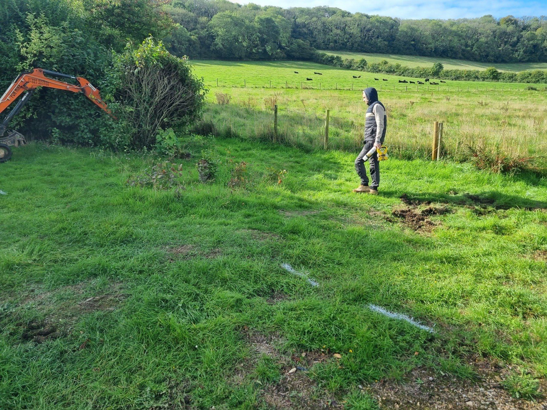A man is standing in a grassy field next to an excavator.