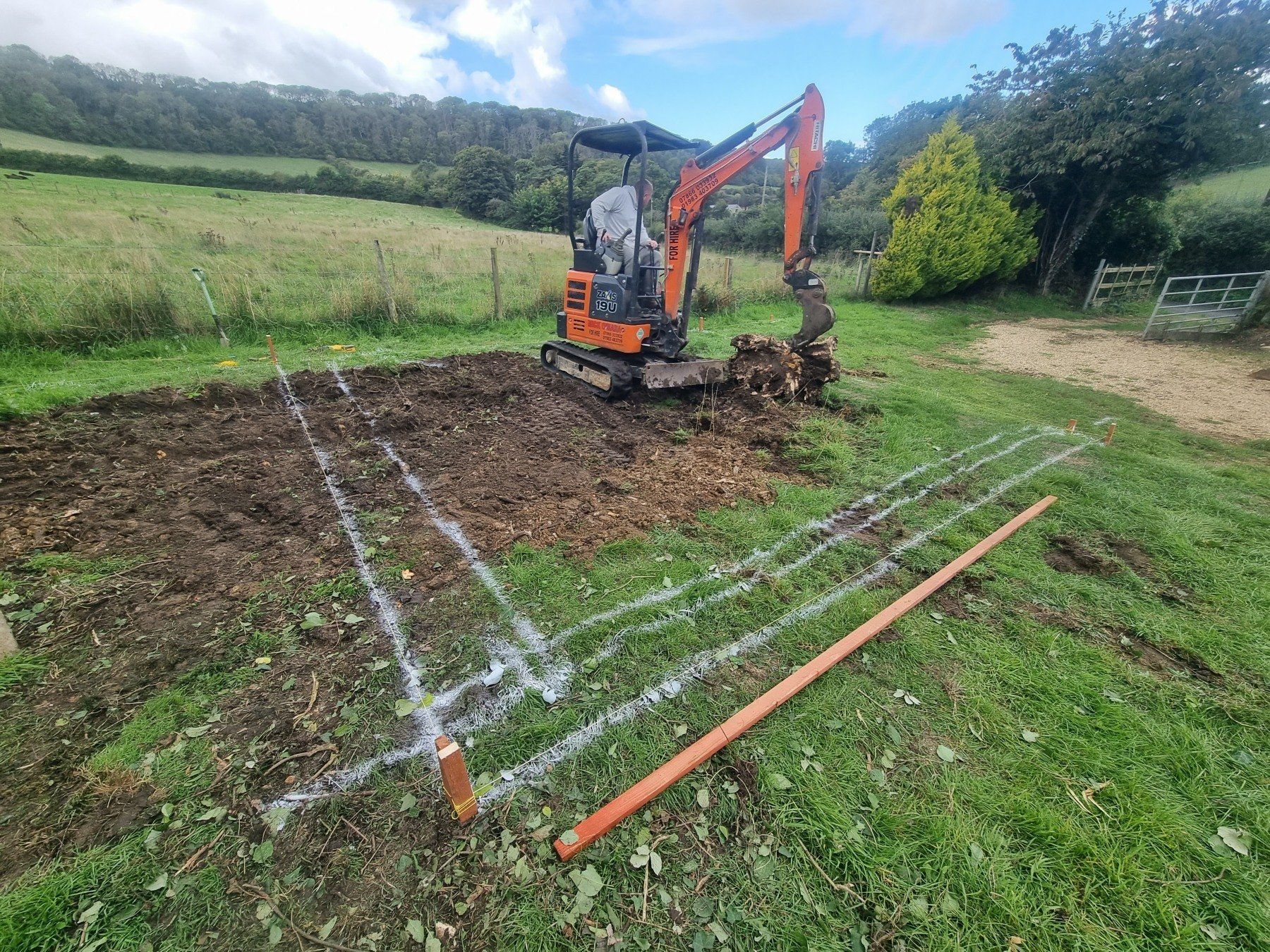 A small excavator is digging a hole in a grassy field.