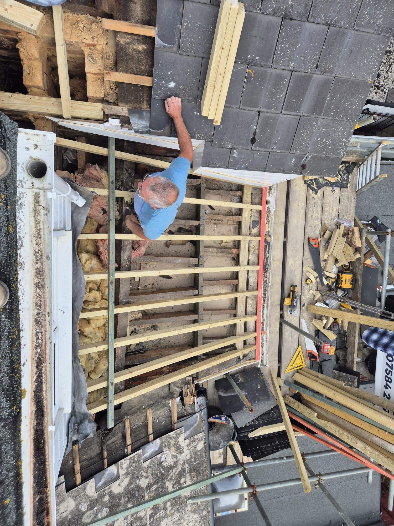 Man working on a roof, surrounded by construction materials, visible beams, and tiles.