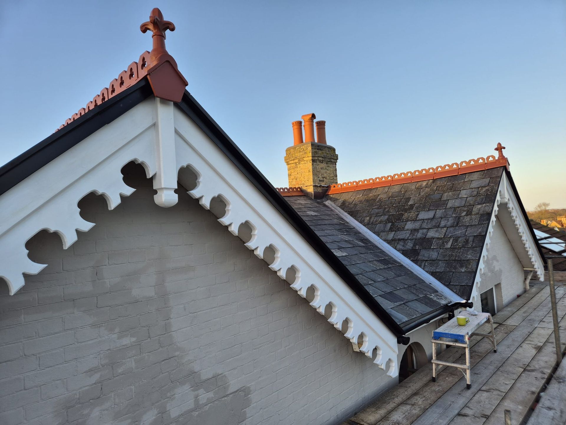Gabled roof with decorative white trim, red tile accents, and brick chimney against a blue sky.