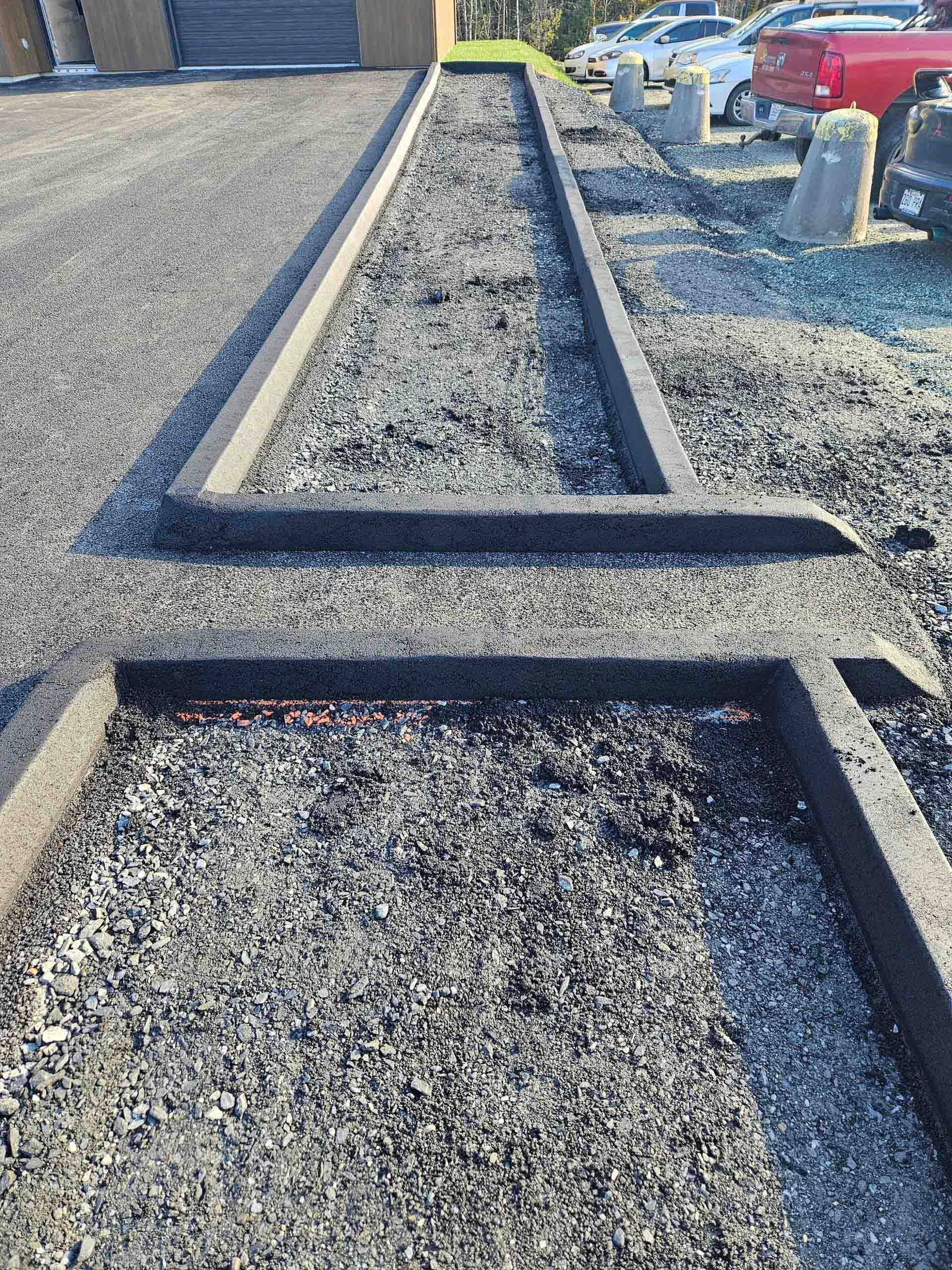 Raised gravel border and rectangular gravel beds beside a paved parking lot with parked cars.