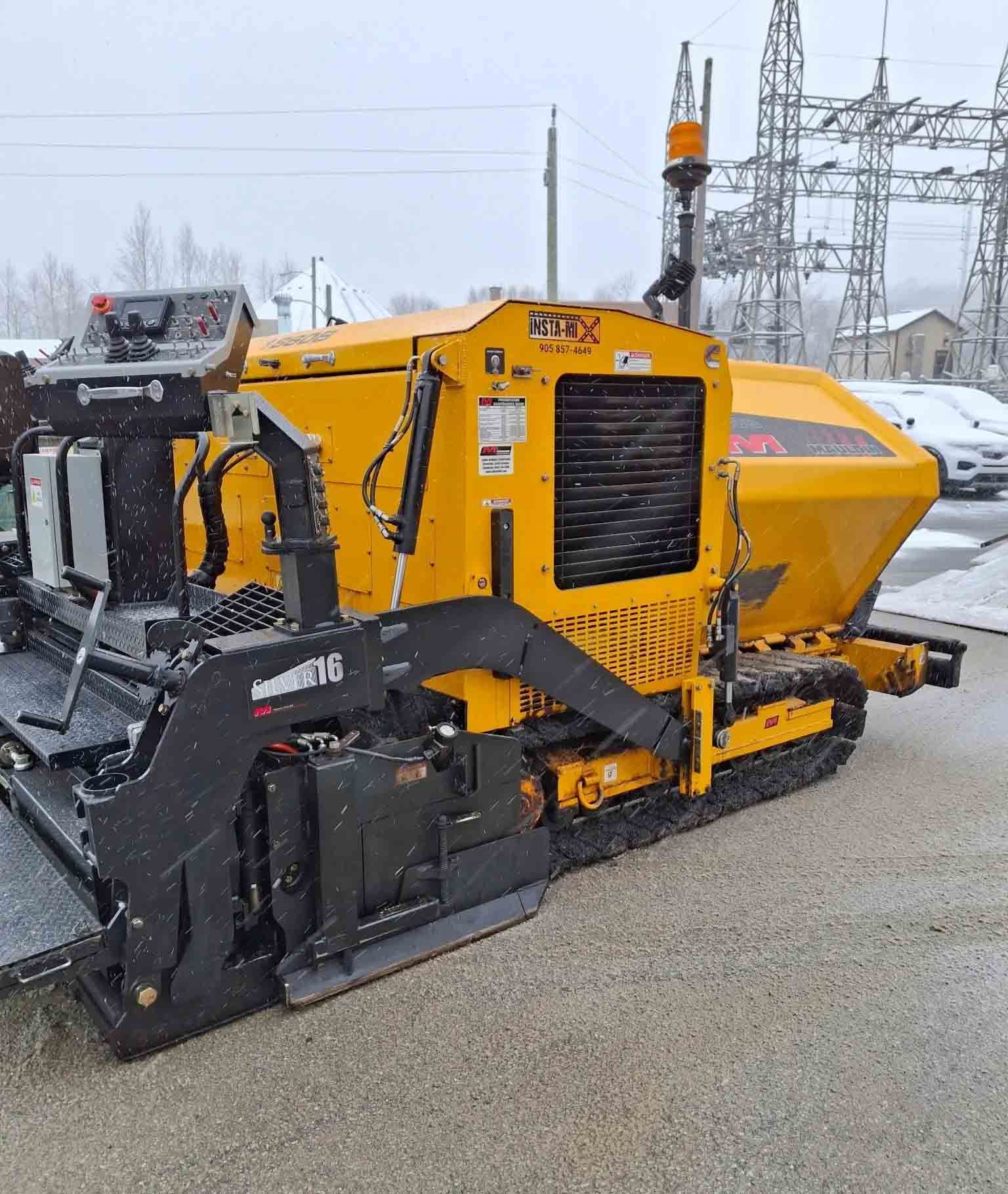 Engin de chantier jaune à chenilles, stationné à l'extérieur dans la neige près de lignes électriques.