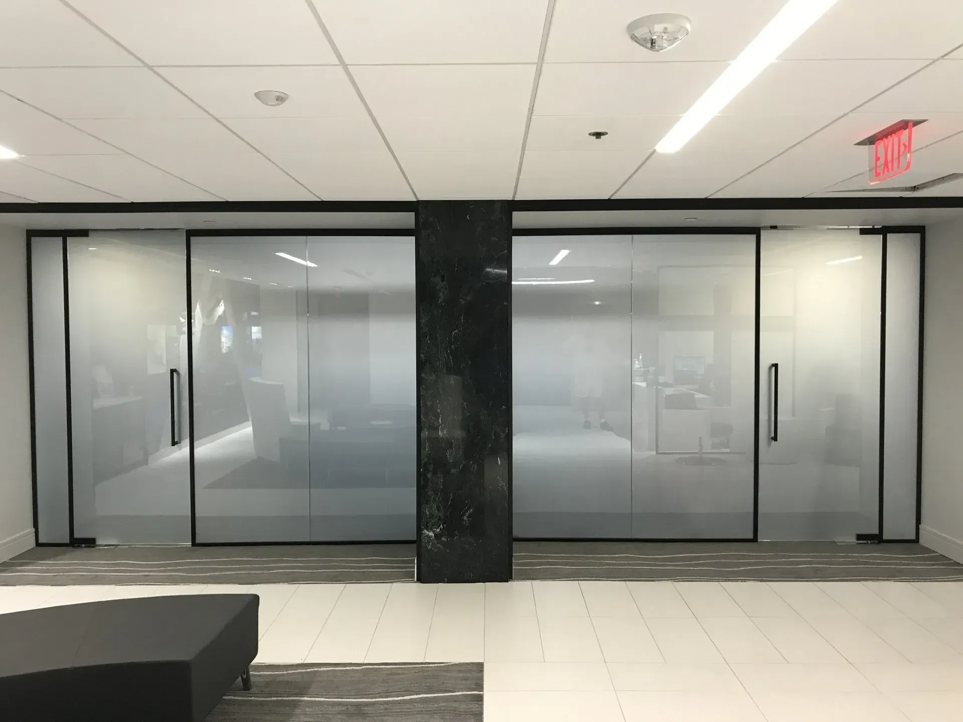 A room with a lot of glass doors and a red exit sign.