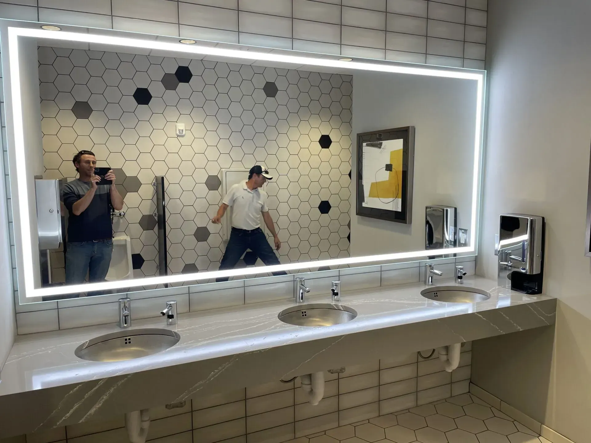 Two men are taking a picture of themselves in a bathroom mirror.