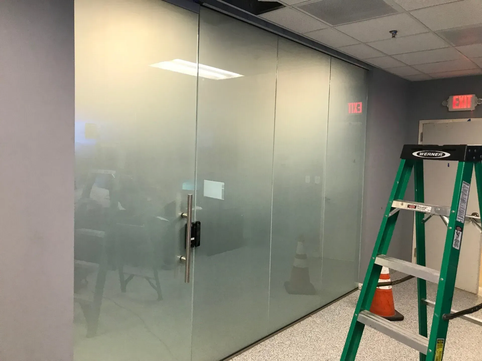 A ladder is sitting in a hallway next to a glass wall.