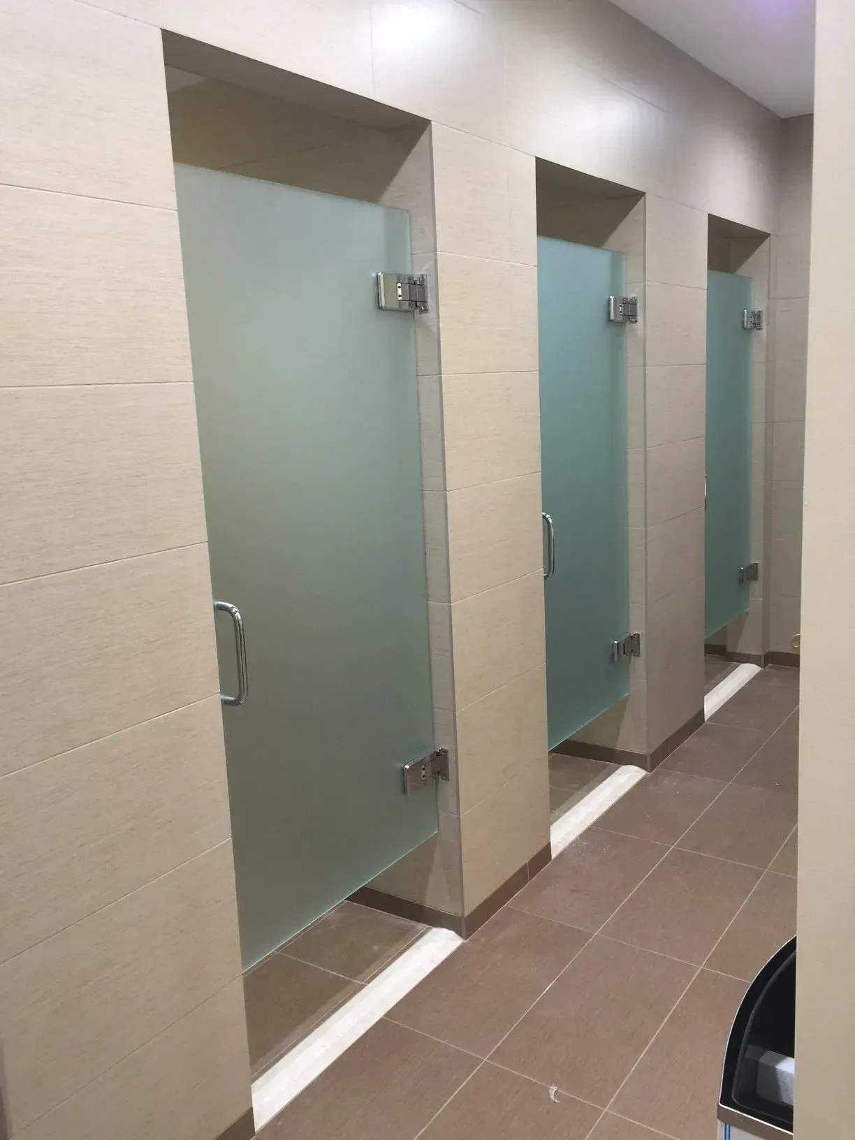 A row of shower stalls with frosted glass doors in a bathroom.