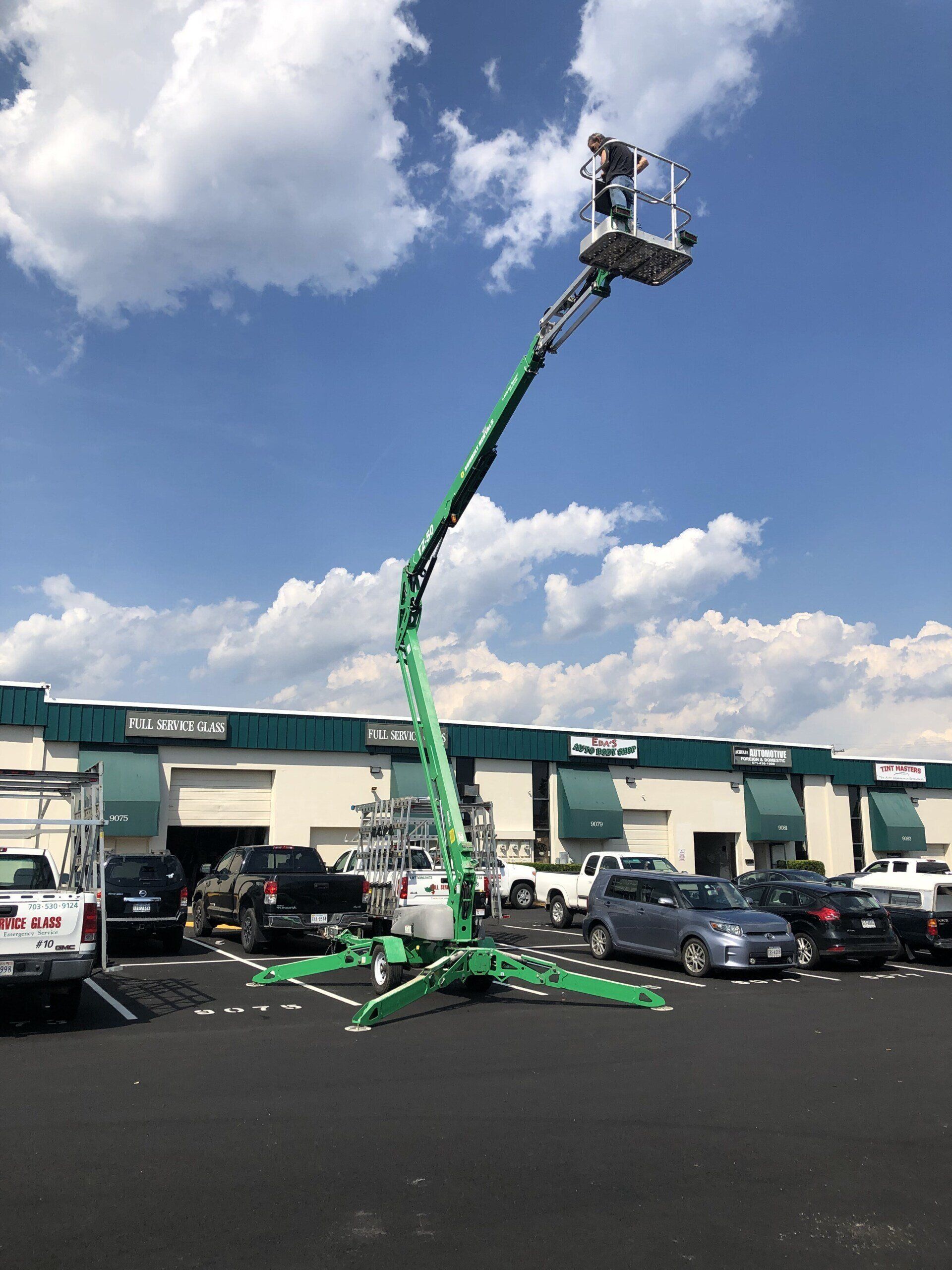 A green crane is in a parking lot in front of a building