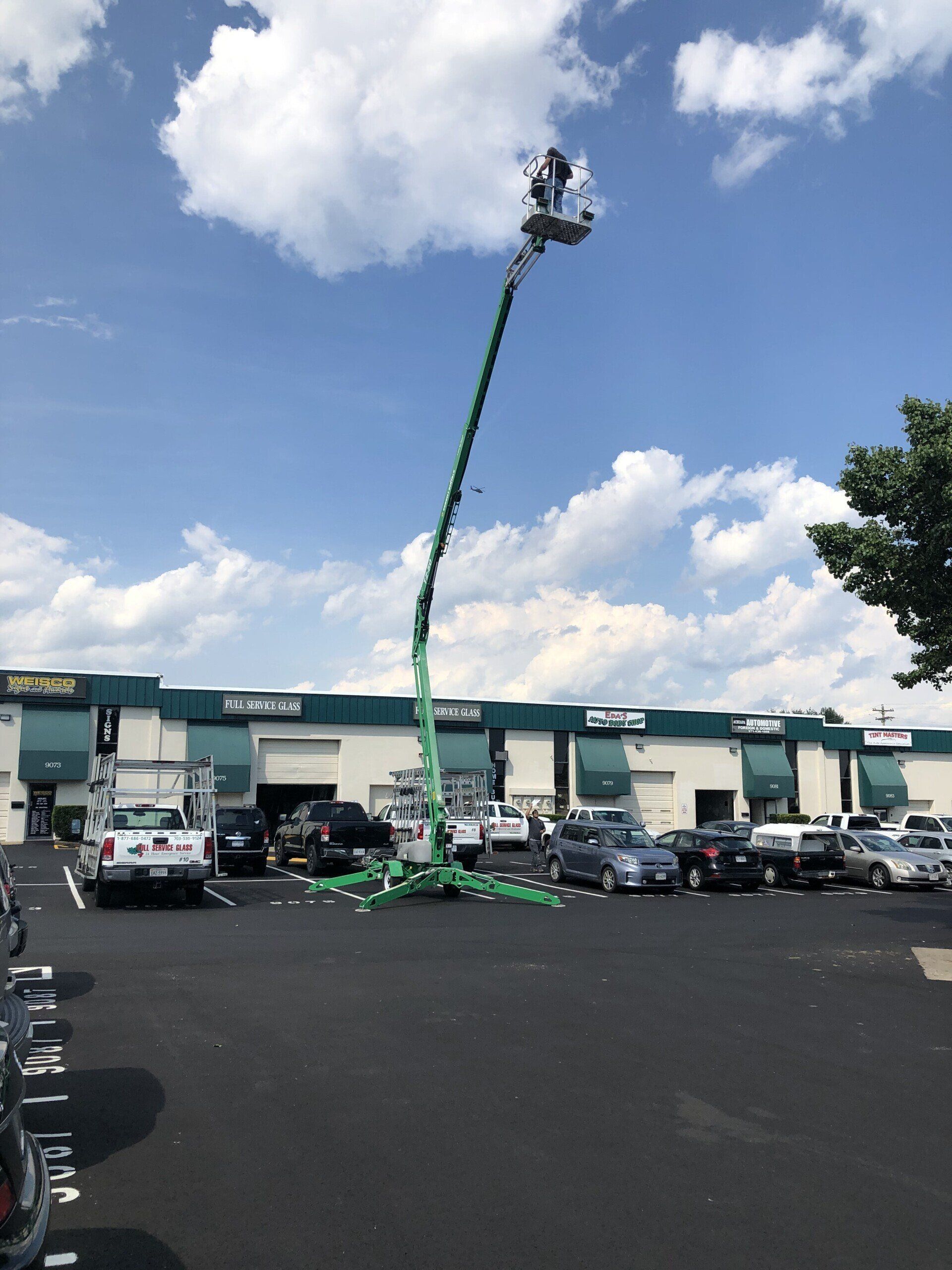 A green crane is in a parking lot in front of a building