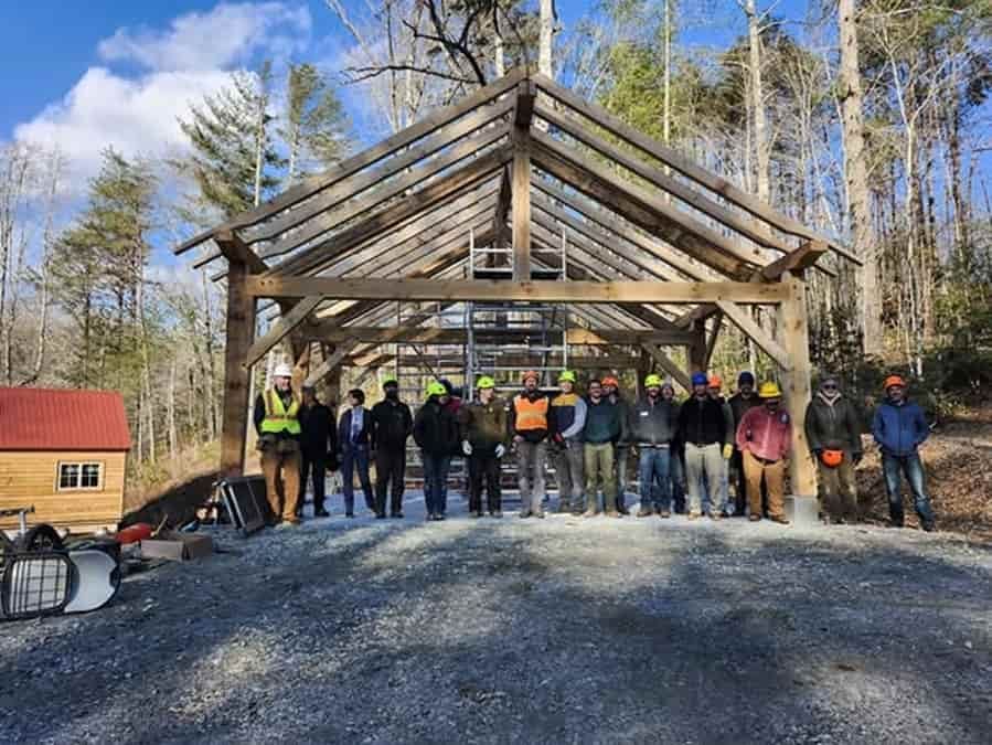 The Heartwood on the Road class of 2026 stands lined up in front of the 24' x 24' timber frame carport that they built