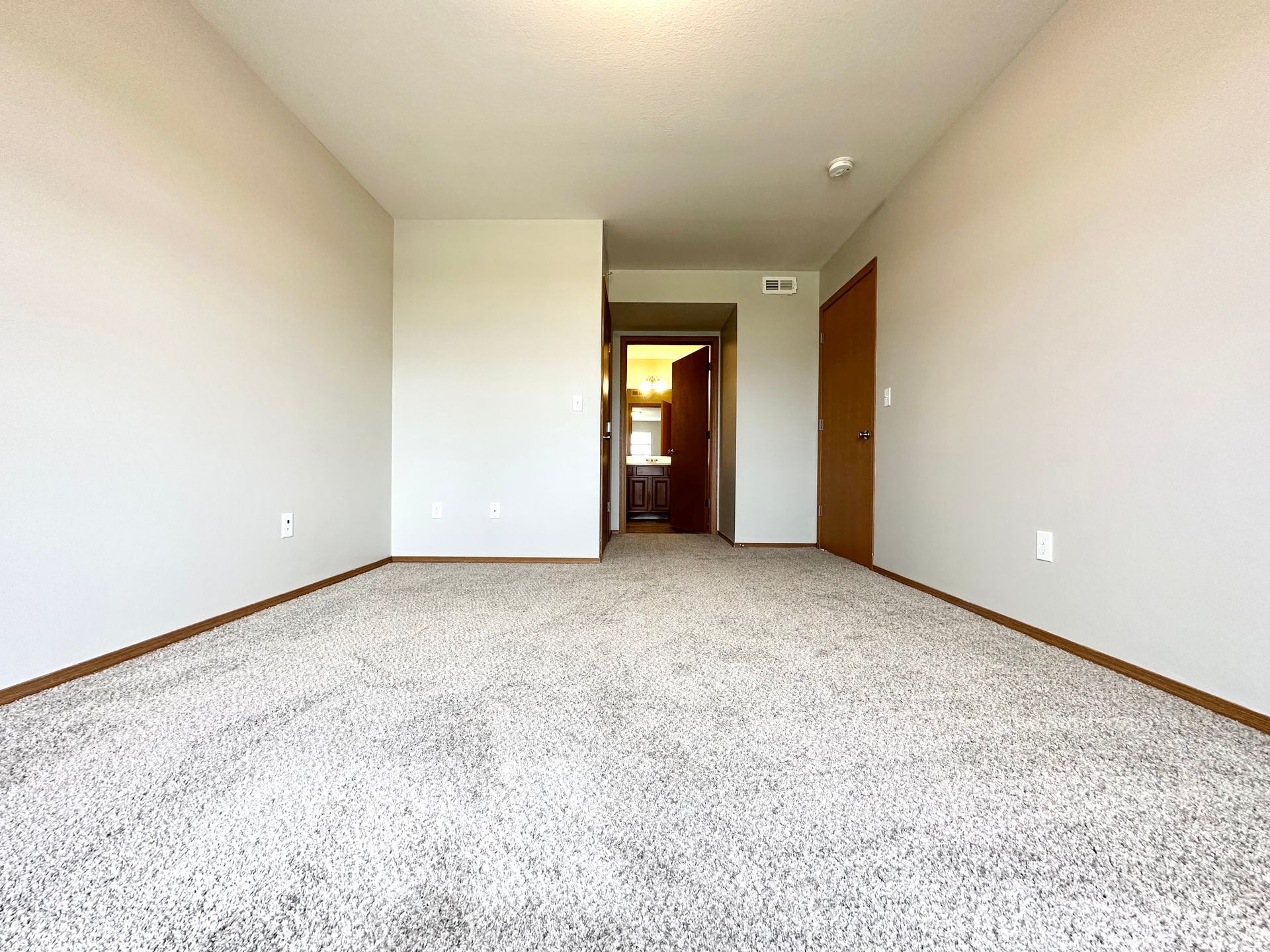 an empty bedroom with a carpeted floor and white walls .
