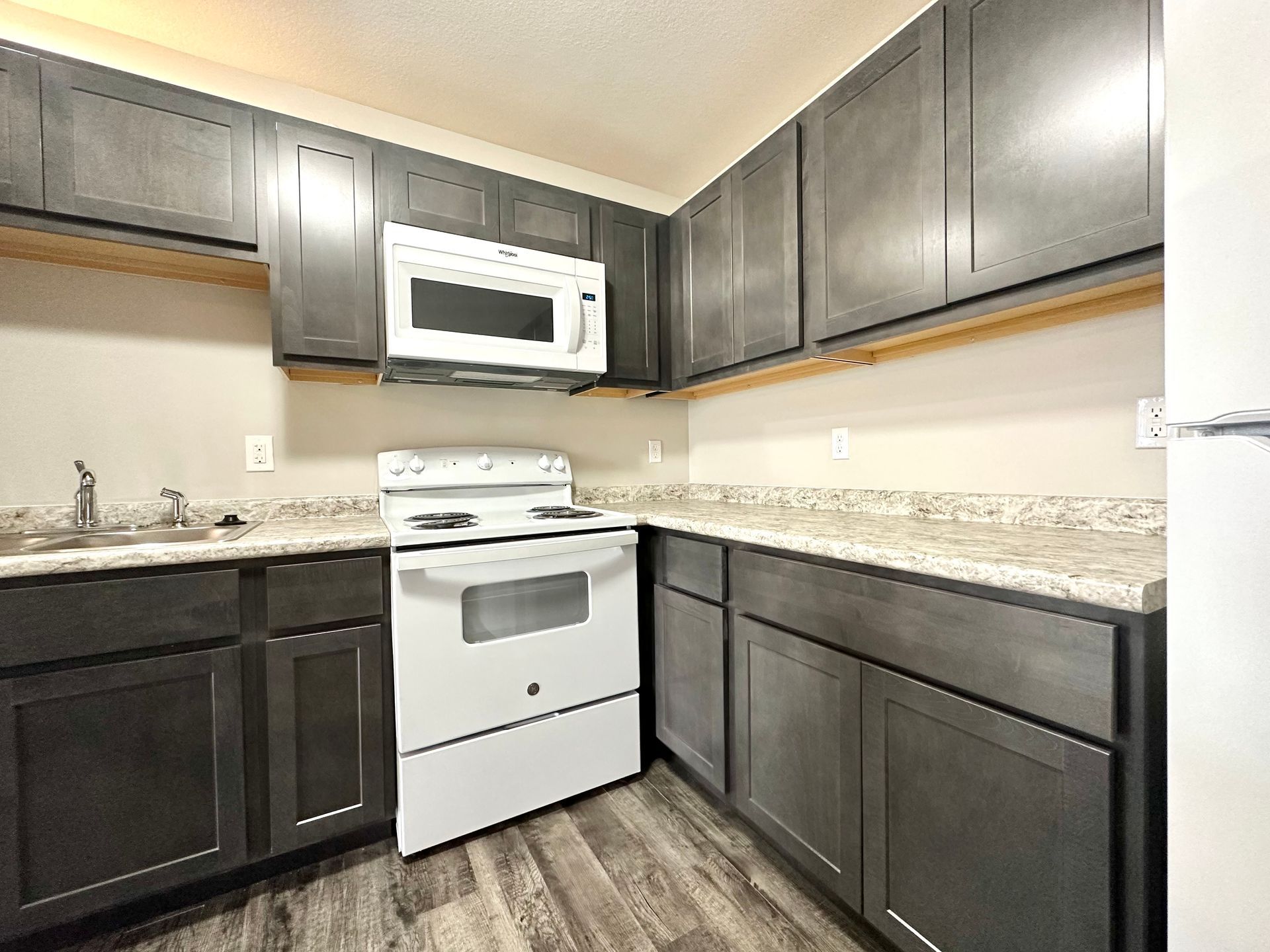 a kitchen with black cabinets , a white stove , a microwave , and a refrigerator .