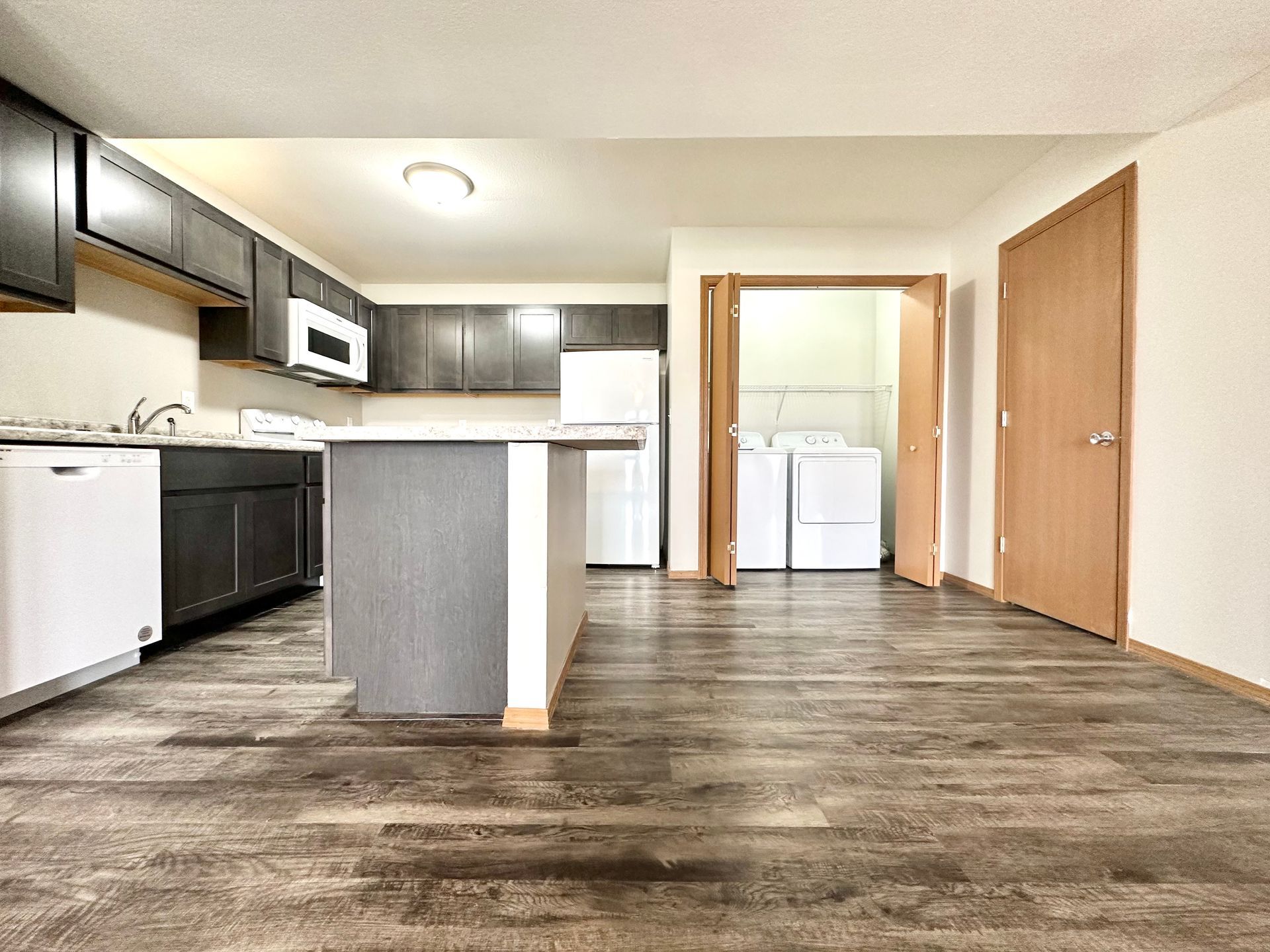a kitchen with wooden floors and a laundry room in the background .