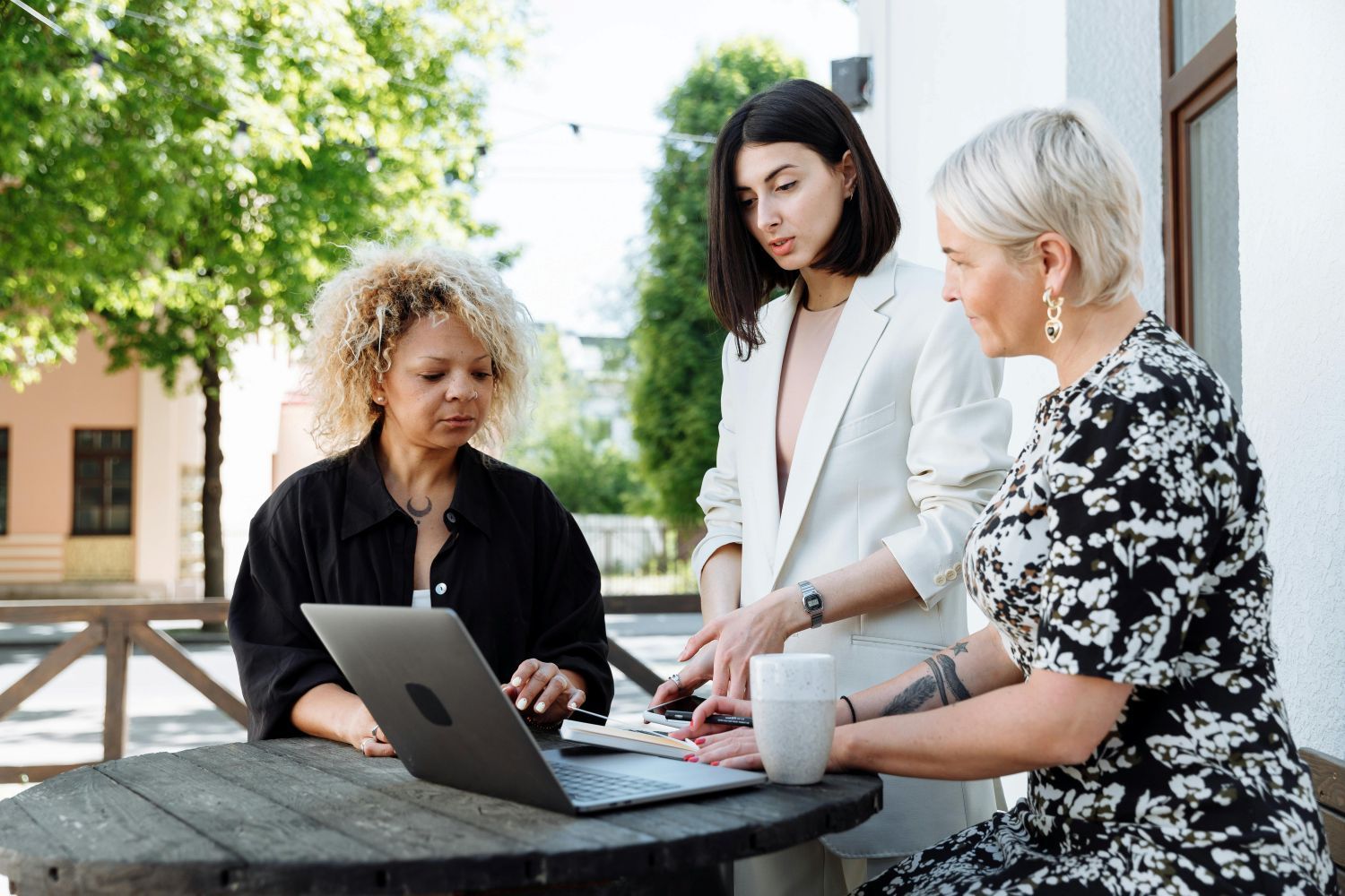 Three people working together around a laptop outdoors. One points, discussing the screen.