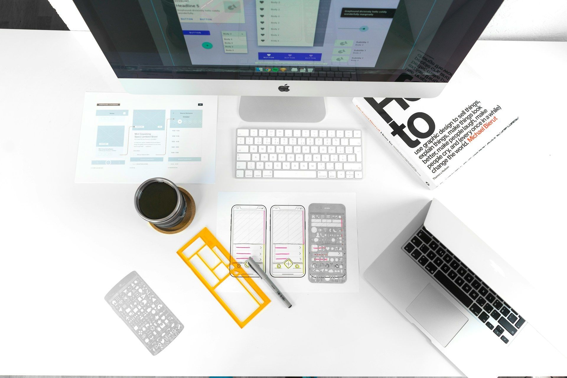 Workspace with computer, phone, and design tools arranged on a white desk.