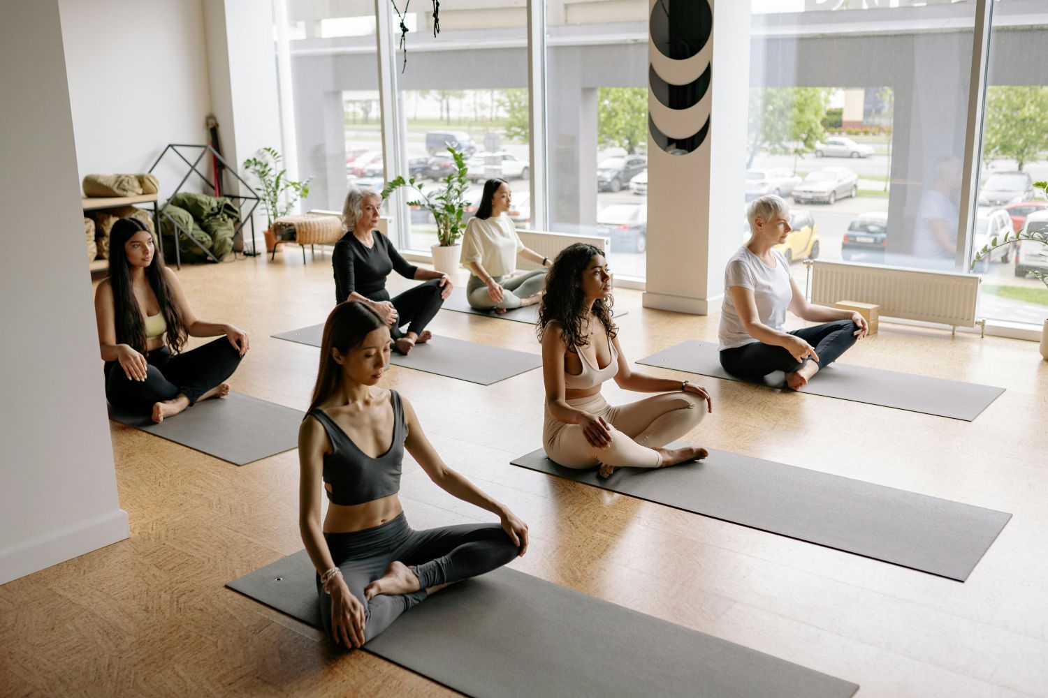 People meditating on yoga mats in a sunlit studio, windows in background.