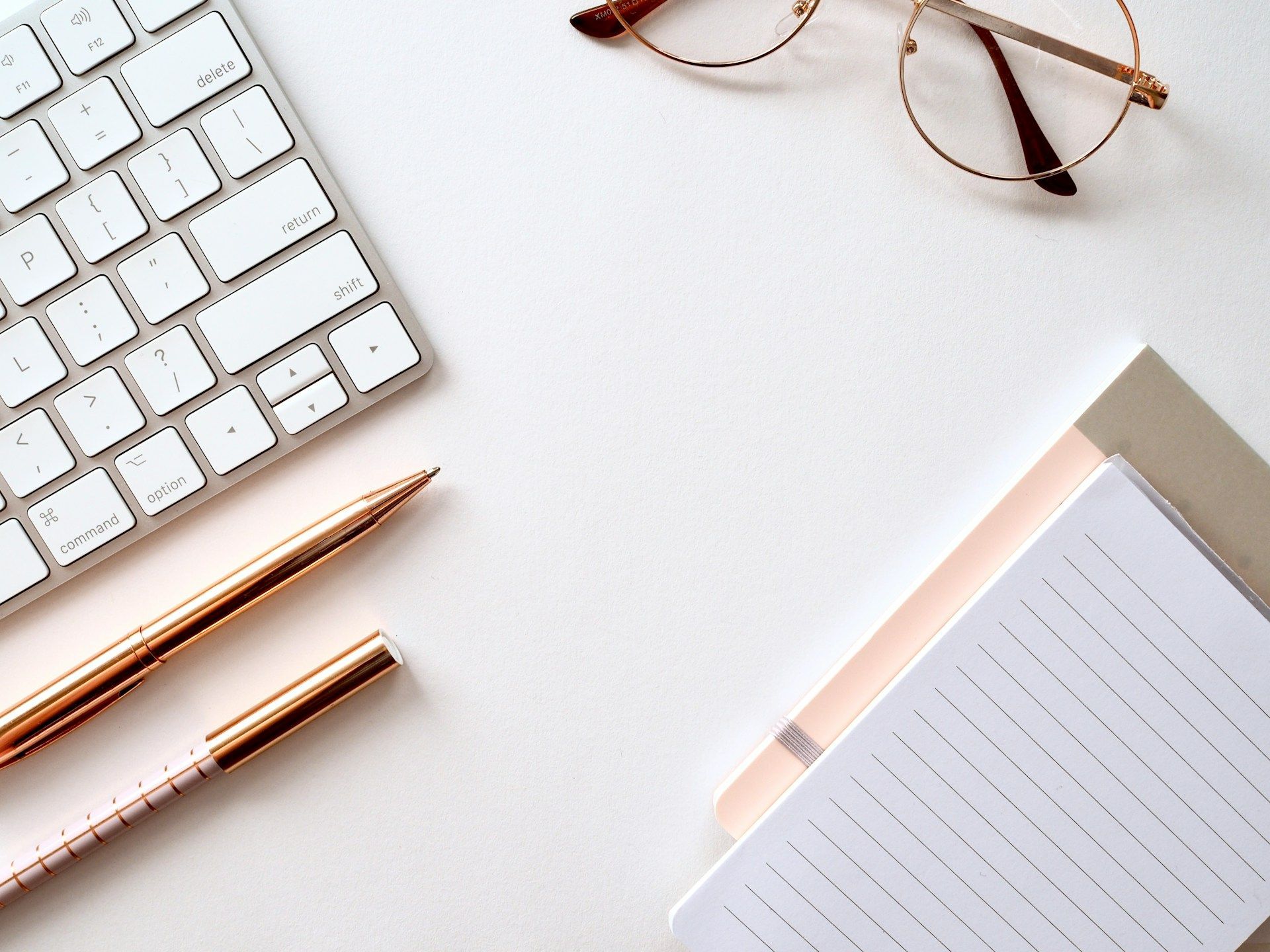 White desk with keyboard, pens, notebook, and glasses arranged, creating a workspace.