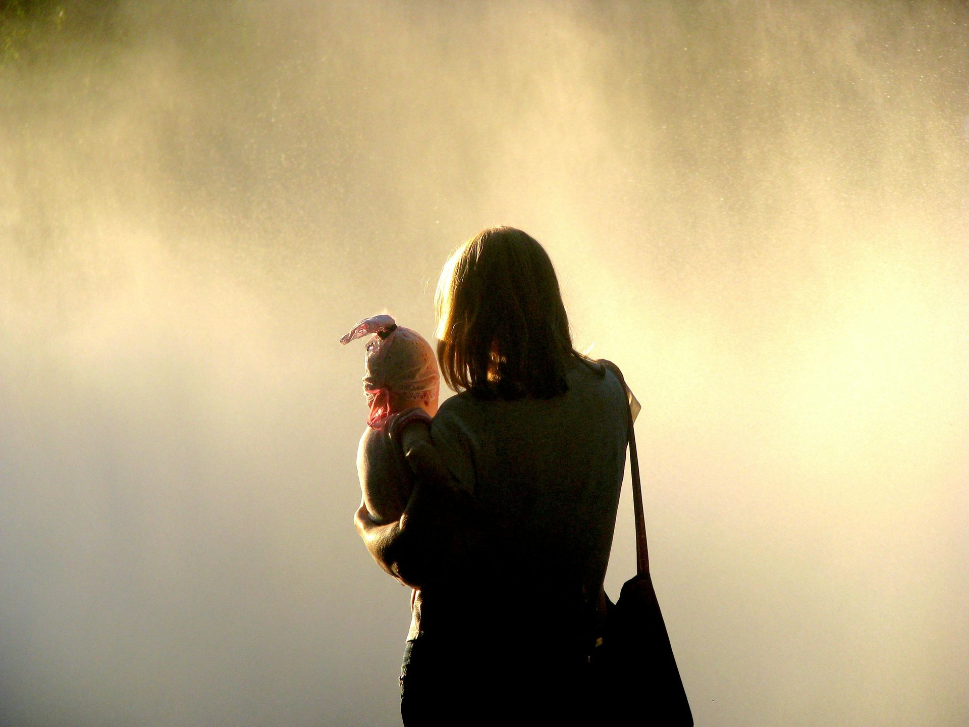 Woman holding baby, silhouetted against a hazy, golden background.