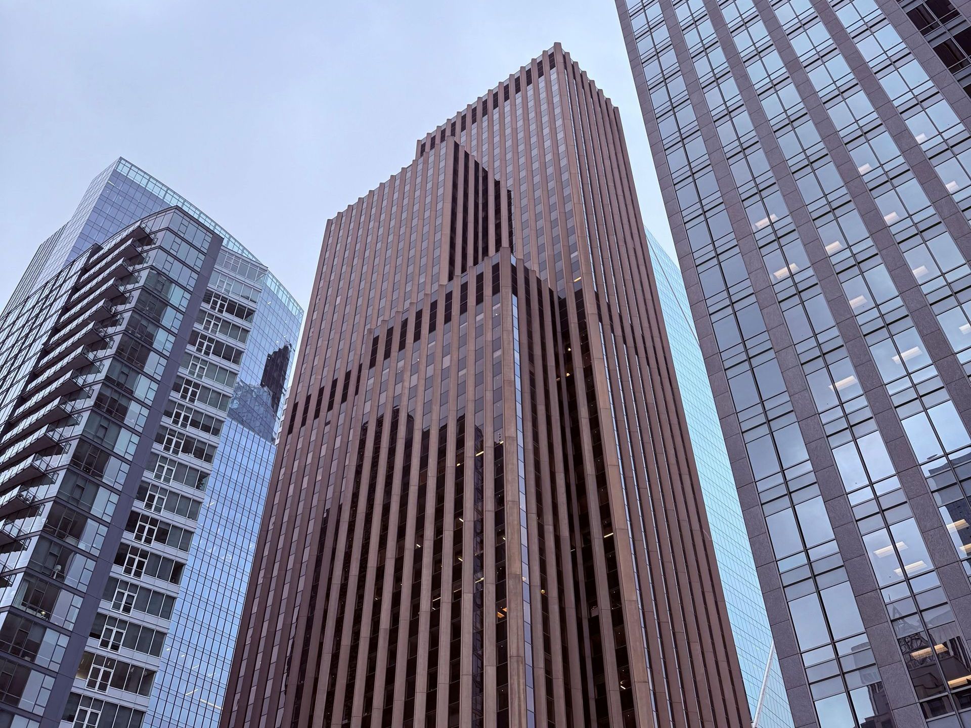 Tall brown and glass skyscrapers under a cloudy sky, viewed from below.